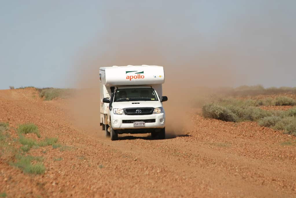 A 4WD campervan driving down a red dusty road.