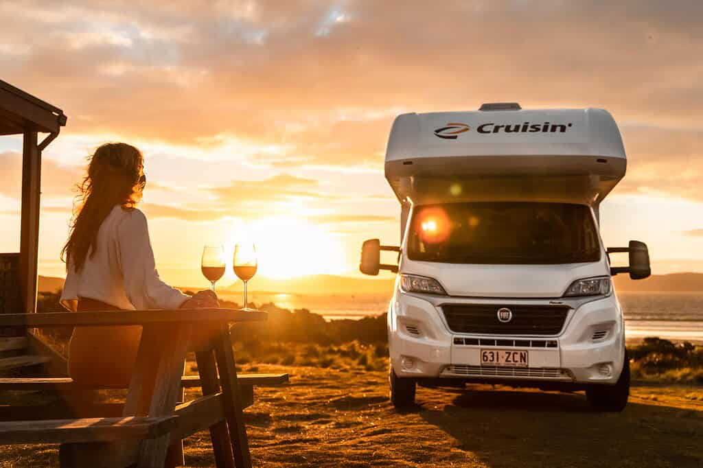 Sunset with a woman enjoying wine on outdoor terrace next to a campervan in Australia.