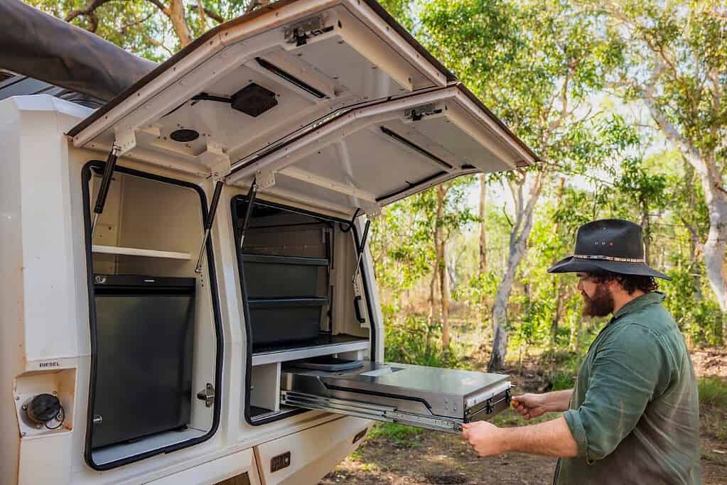 Traveller pulling out a slide-out kitchen drawer beside the fridge in a 4WD camper storage compartment