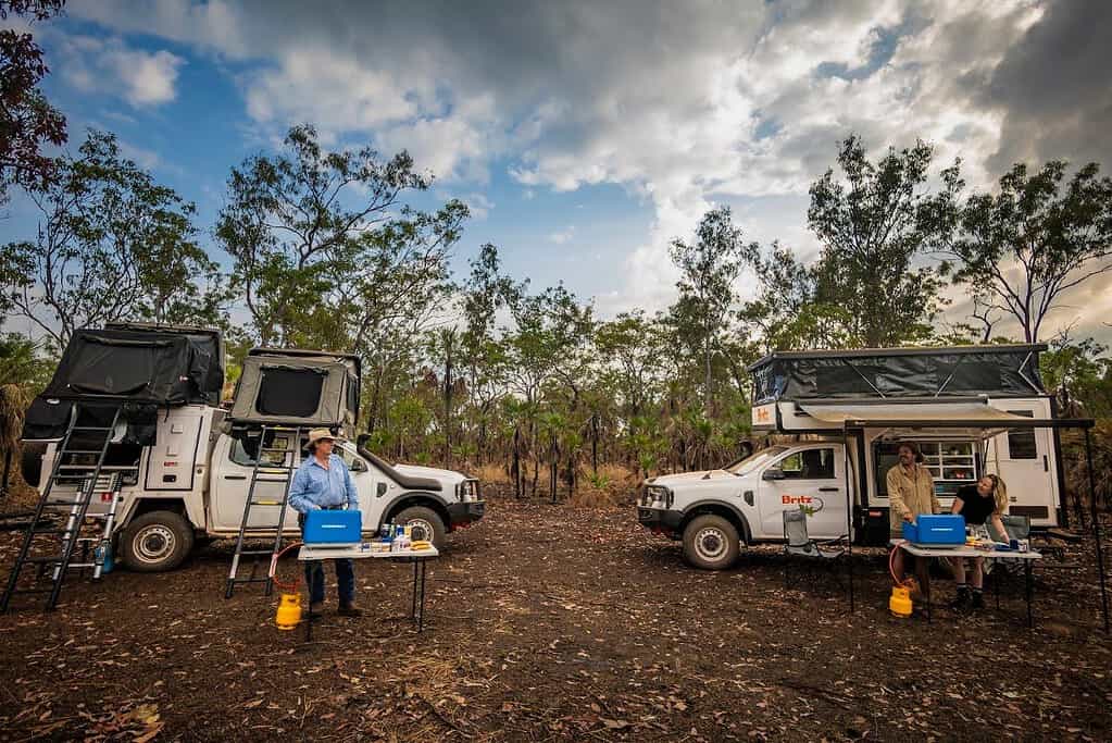 Two 4WD campers with rooftop tents set up at a bush campsite with outdoor tables and camping gear