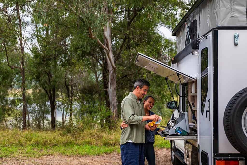 Couple preparing a drink at the rear slide-out kitchen of an Apollo Adventure Camper 4WD