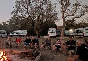 Escorted motorhome tour group around a campfire with Maui motorhomes at camp