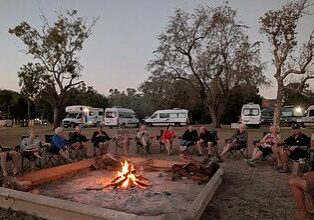 Escorted motorhome tour group around a campfire with Maui motorhomes at camp