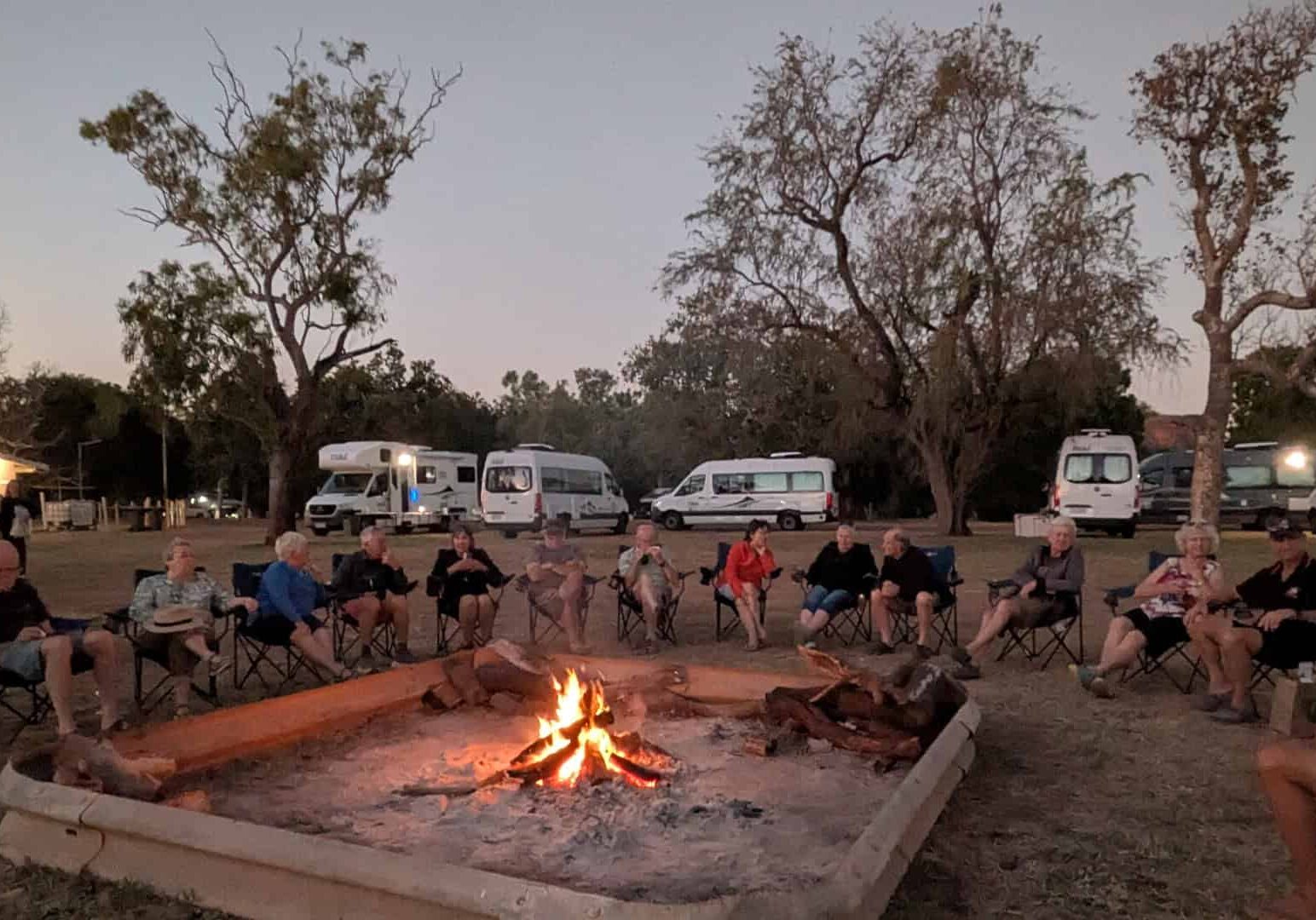Escorted motorhome tour group around a campfire with Maui motorhomes at camp